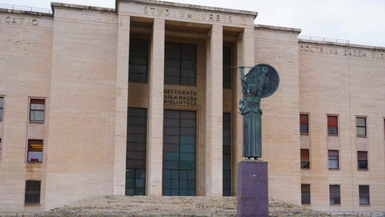 A statue Minerva the goddess of wisdom holding a sword and a shield in front of the biggest and most central building in La Sapienza