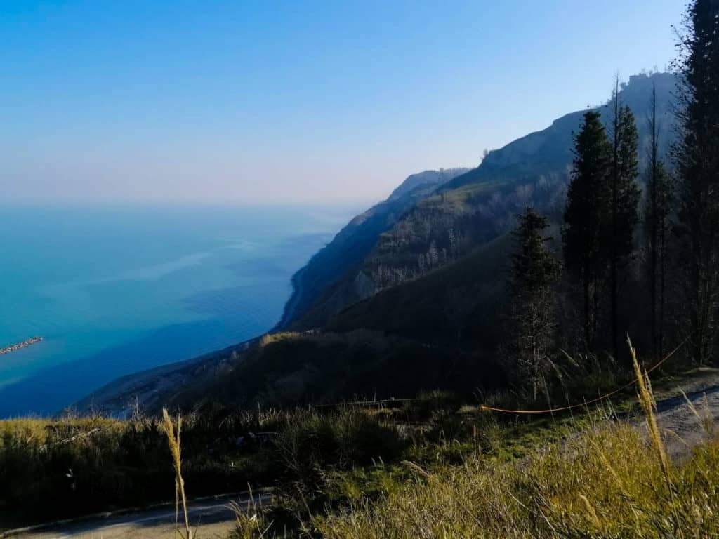 A body of water is seen on the left with a clif on the right, it's a scenic view of Pesaro located in Marche Region