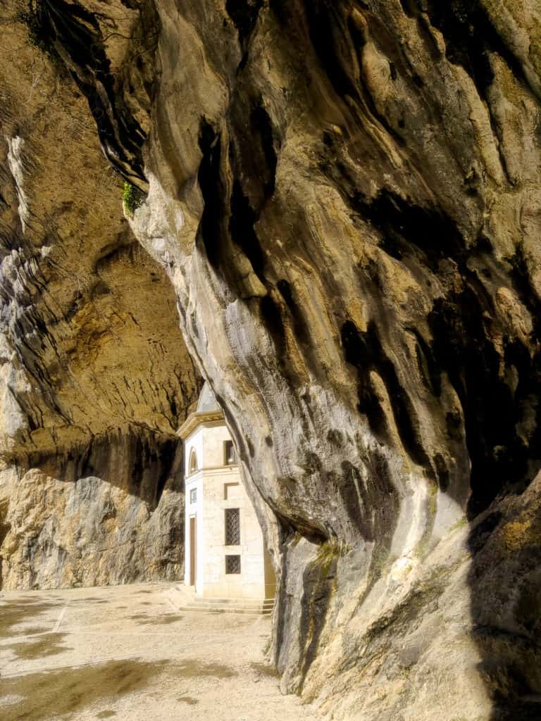 Inside of a cave with a small sanctuary seen behind a cave wall. It is Santa Maria Sanctuary located in Marche region